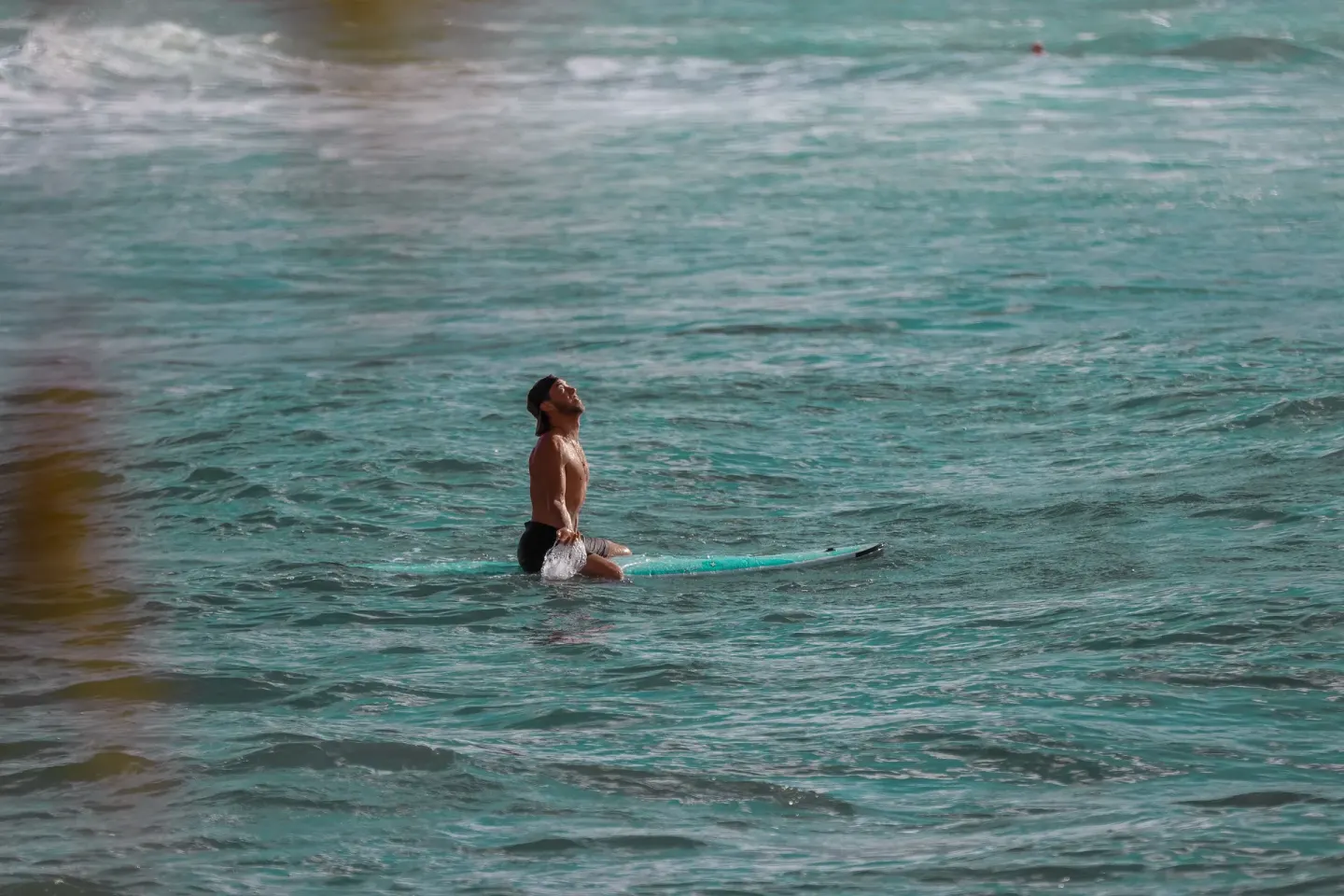 Surfer sitting on a board in turquoise ocean water near Ohia Waikiki Studio Suites.