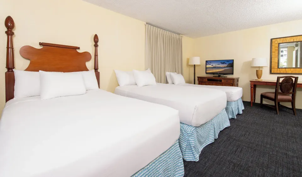 City View Deluxe room with three beds, TV, desk, and mirror at Ohia Waikiki Studio Suites.