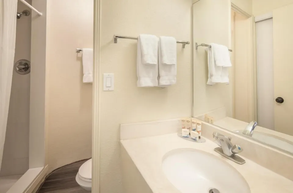 Bathroom with sink, mirror, towels, and shower at Ohia Waikiki Studio Suites.