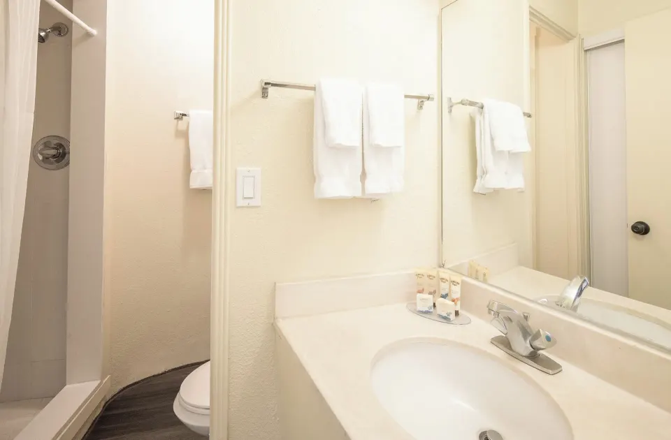 Bathroom vanity, towels, and shower in a Sky View Two room at Ohia Waikiki Studio Suites.
