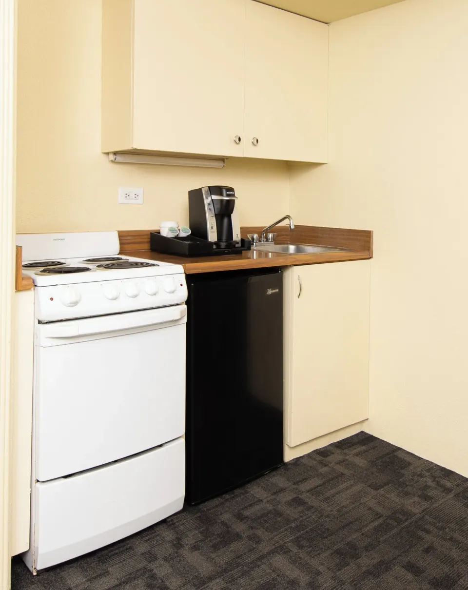 Kitchenette with stove, mini fridge, sink, and coffee maker in a Sky View Two room at Ohia Waikiki Studio Suites.