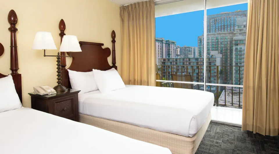 Two beds beside a balcony with city views in a Sky View Two room at Ohia Waikiki Studio Suites.