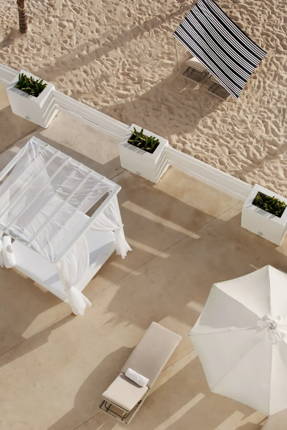 Beach cabana, lounger, and striped shade on the sand at Oleo Cancun Playa Resort.
