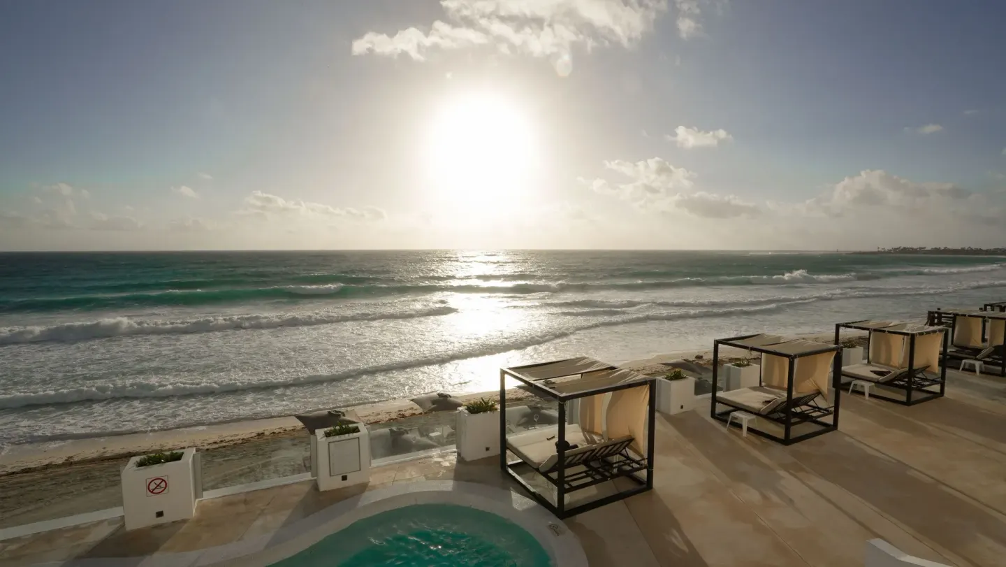 Beachfront sun deck with cabanas and ocean waves at Oleo Cancun Playa Resort.