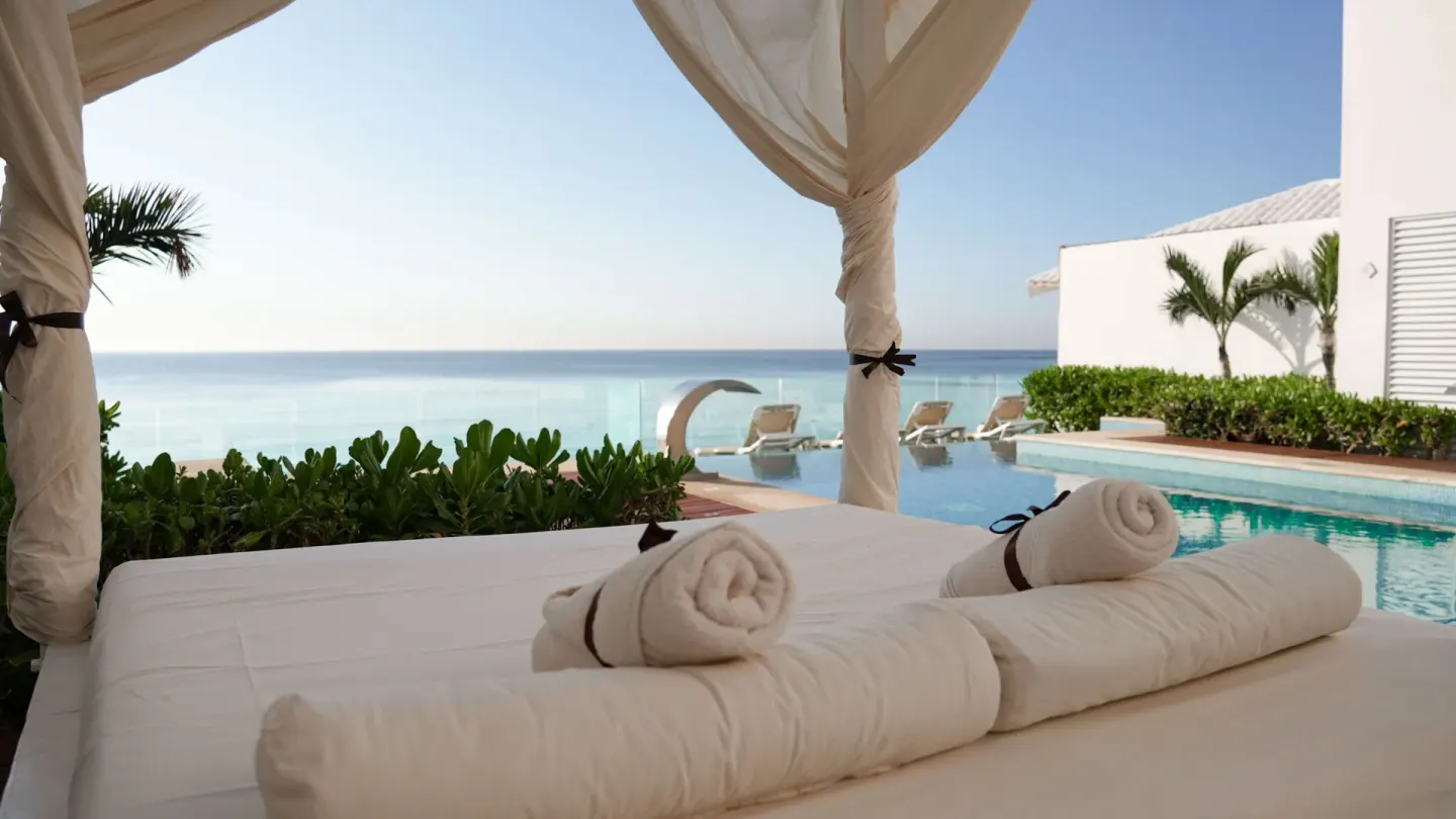 Canopied spa daybed with towels beside the pool at Oleo Cancun Playa Resort.