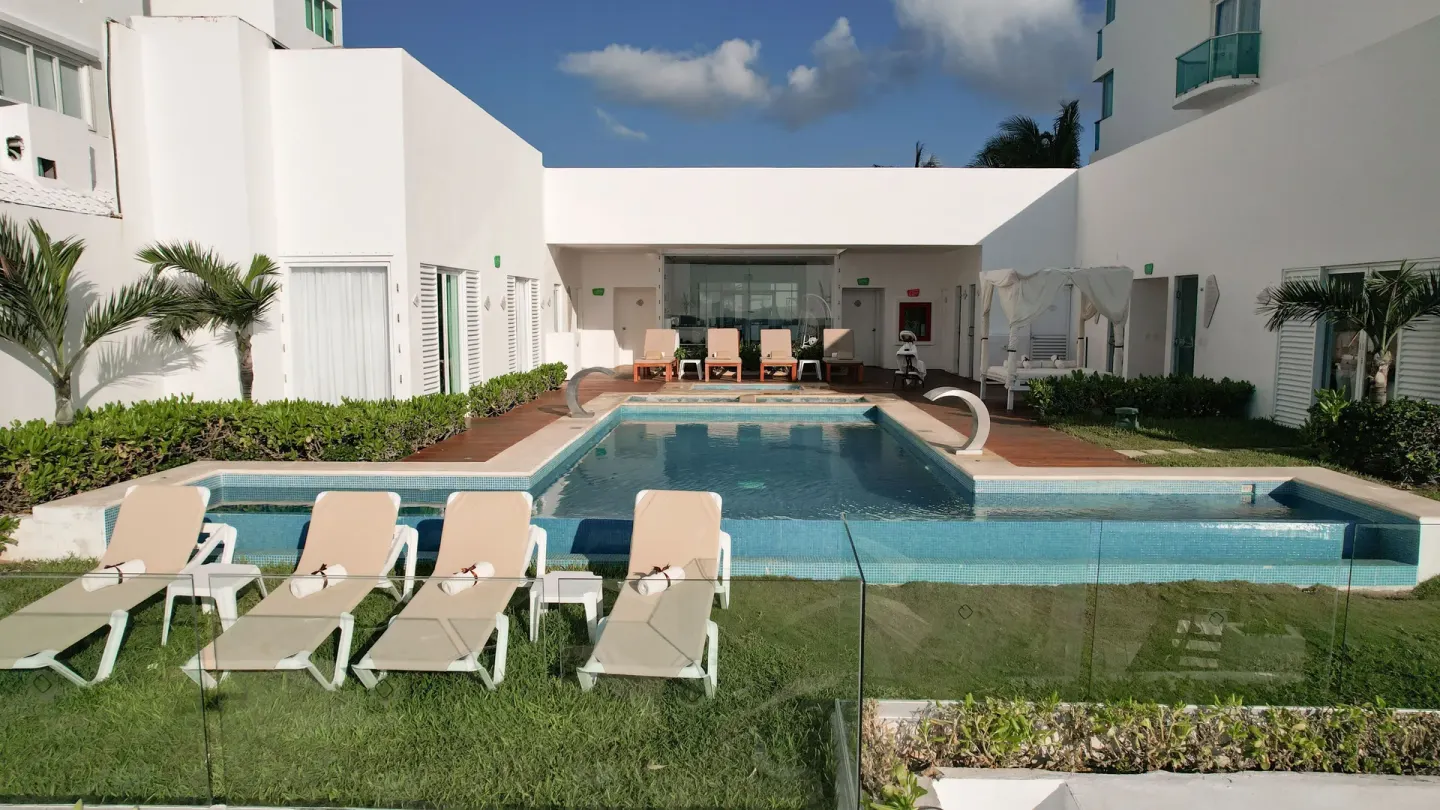Enclosed courtyard pool with loungers and white buildings at Oleo Cancun Playa Resort.