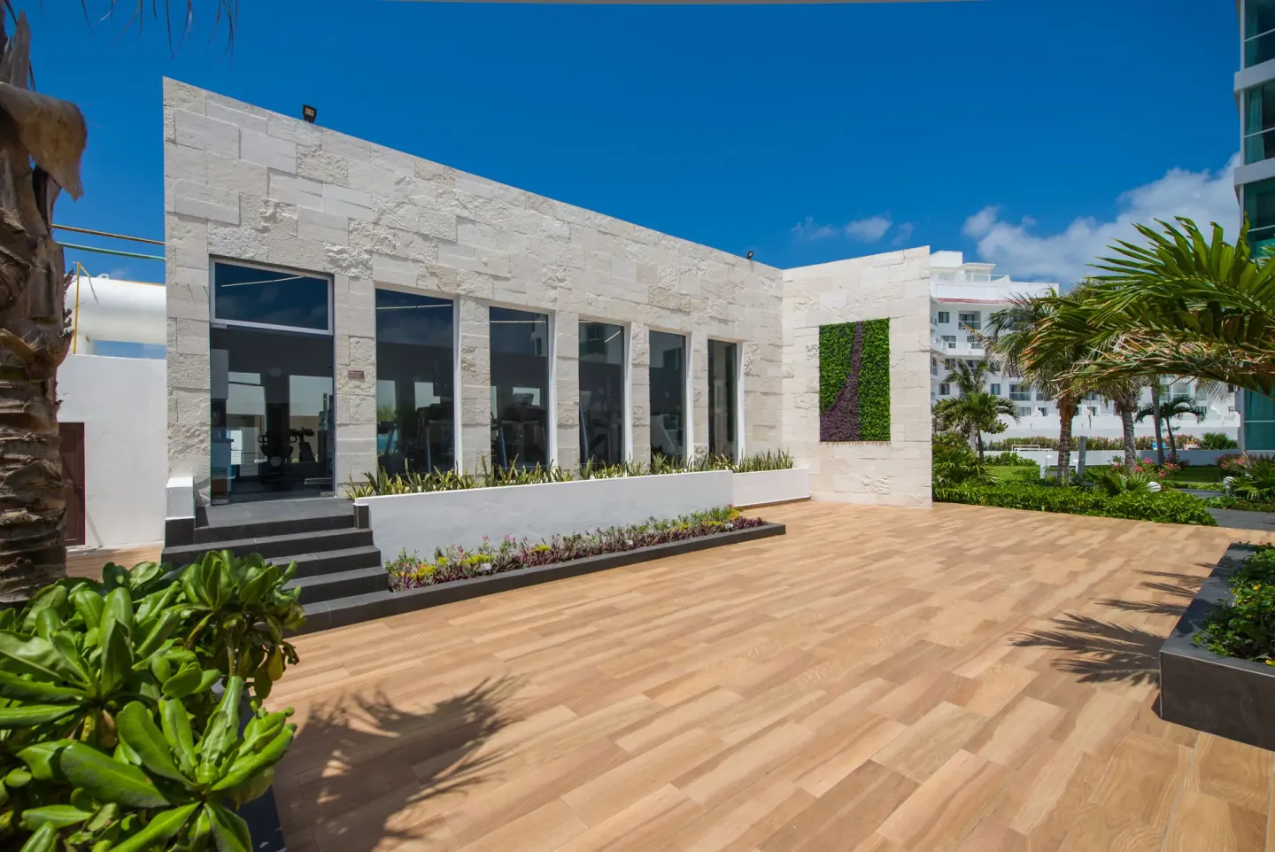 Fitness building terrace with palms and garden beds at Oleo Cancun Playa Resort.