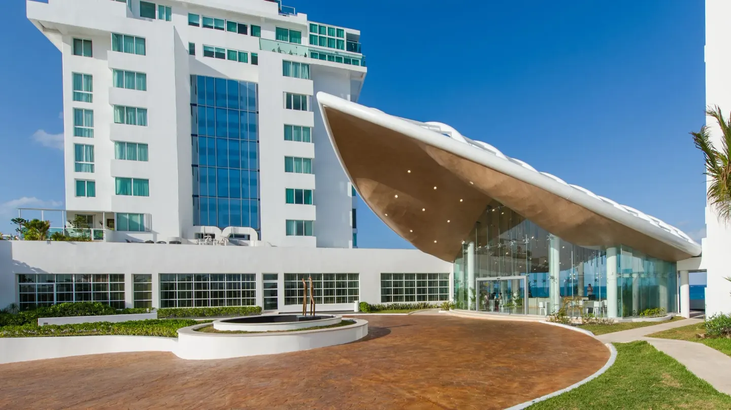Main entrance with sculptural canopy and white tower at Oleo Cancun Playa Resort.