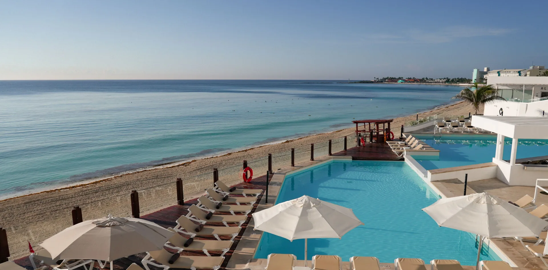 Oceanfront pool with loungers and beach beyond at Oleo Cancun Playa Resort.