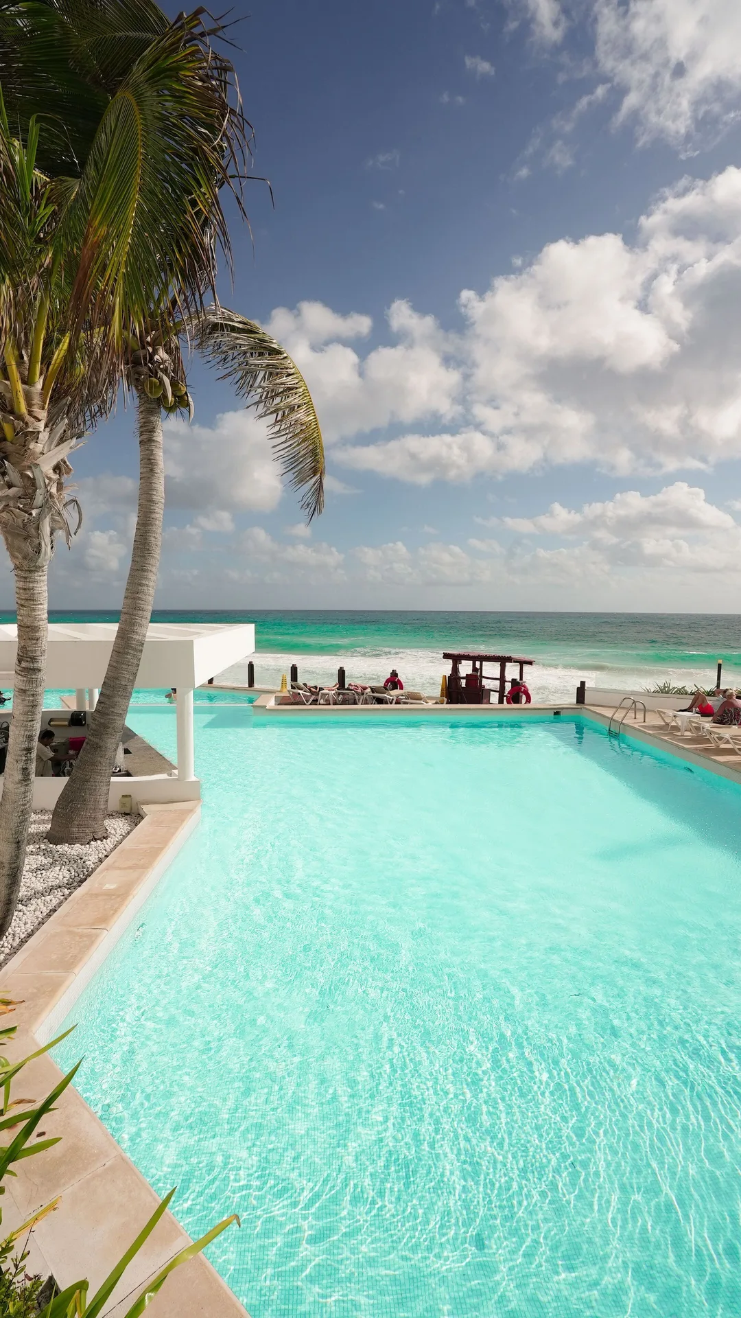 Oceanfront pool with palm trees and beach beyond at Oleo Cancun Playa Resort.