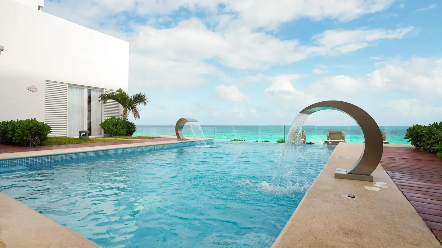 Pool with curved water features and ocean beyond at Oleo Cancun Playa Resort.