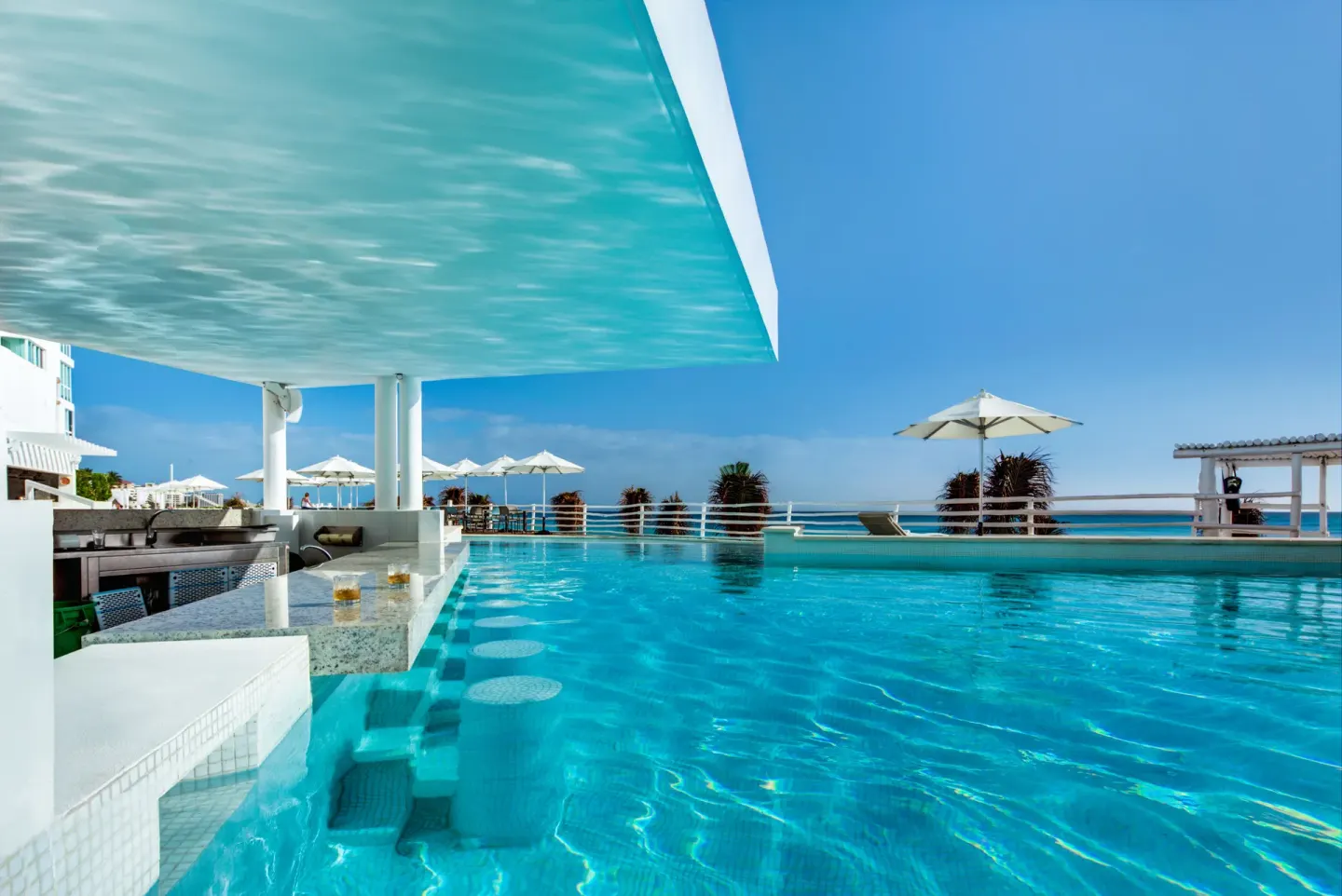 Swim-up pool bar with ocean views and umbrellas at Oleo Cancun Playa Resort.