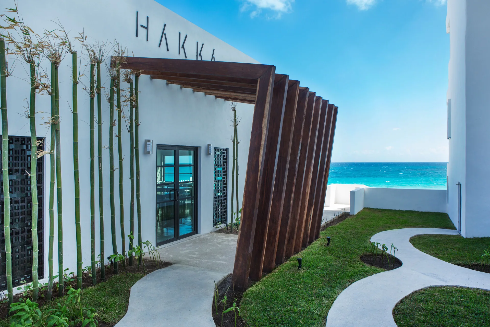 Hakka restaurant entrance with bamboo, wood beams, and ocean beyond at Oleo Cancun Playa Resort.