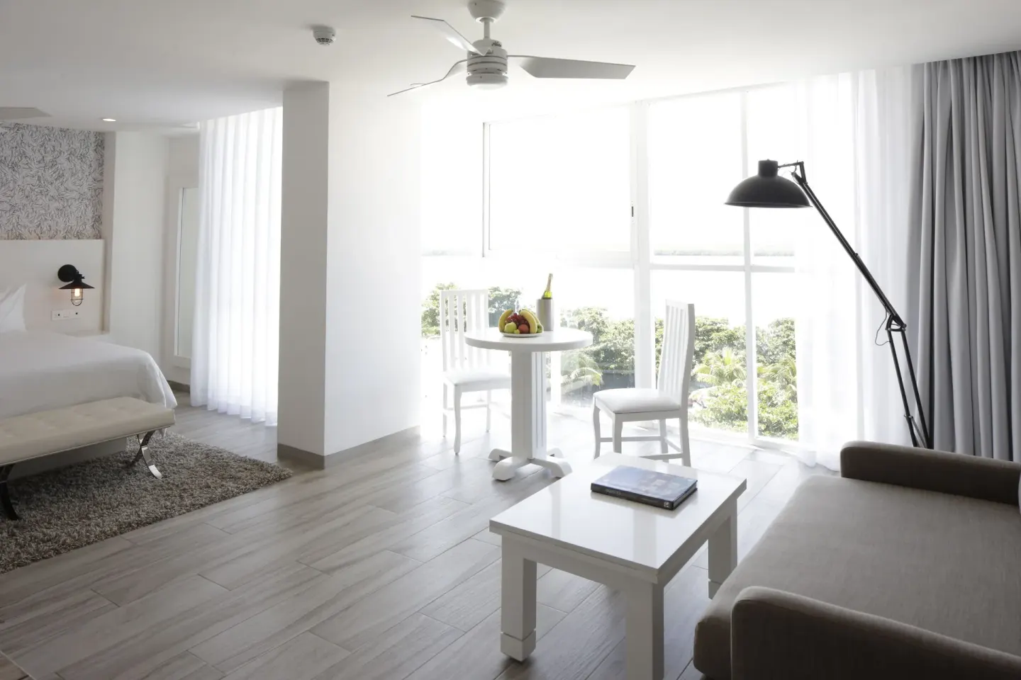 Junior Suite Sunset living area with bed and window seating at Oleo Cancun Playa Resort.