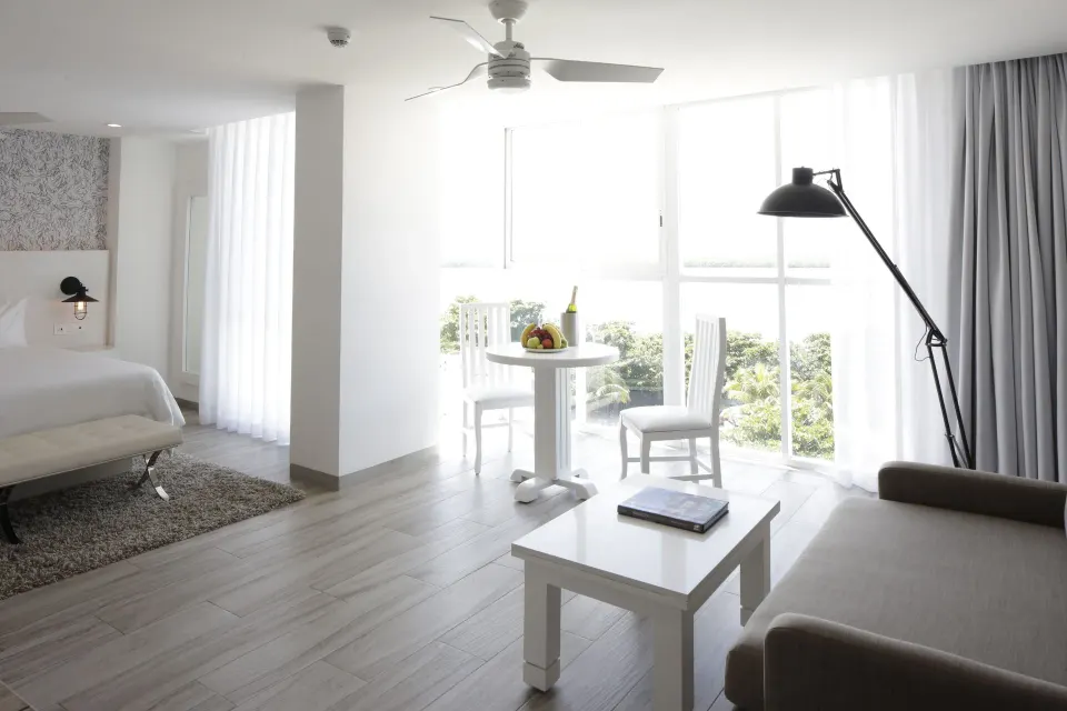 Junior Suite Sunset living area with bed and window seating at Oleo Cancun Playa Resort.
