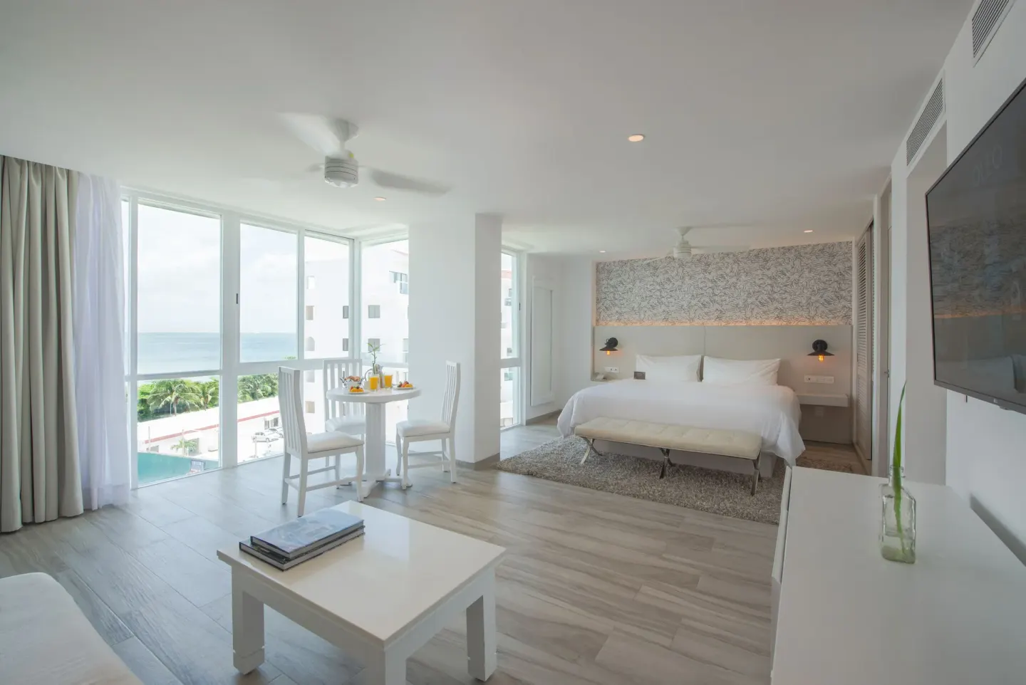 Junior Suite Sunset with king bed, sitting area, TV, and ocean-facing windows at Oleo Cancun Playa Resort.