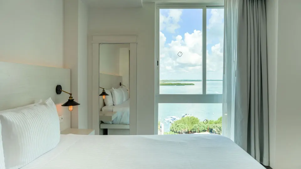 Junior Suite Sunset bed beside a large window with water views at Oleo Cancun Playa Resort.