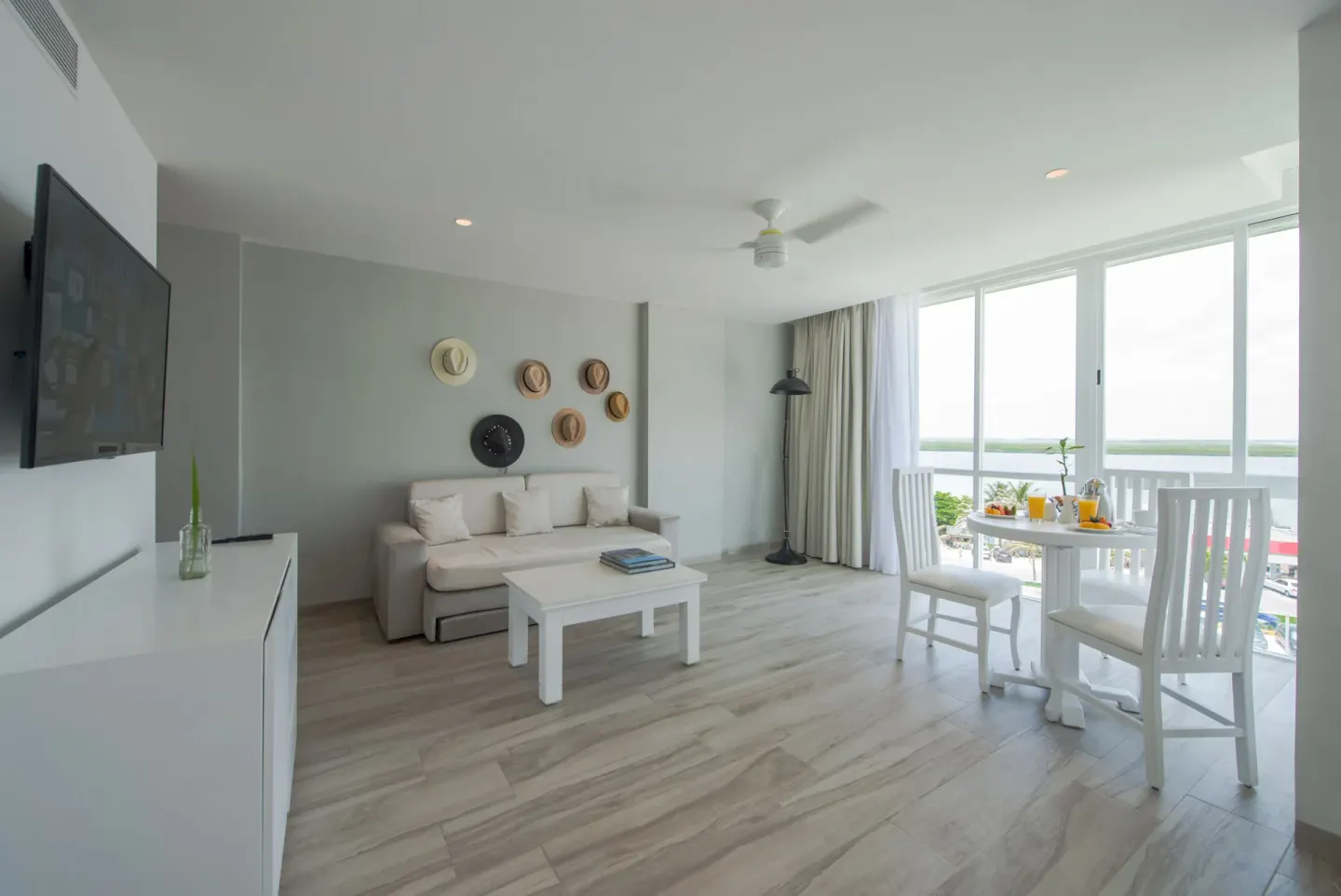 Junior Suite Sunset lounge with sofa, TV, and window dining table at Oleo Cancun Playa Resort.