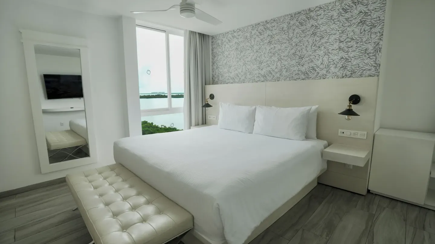 Standard Room king bed with bench and tall mirror at Oleo Cancun Playa Resort.