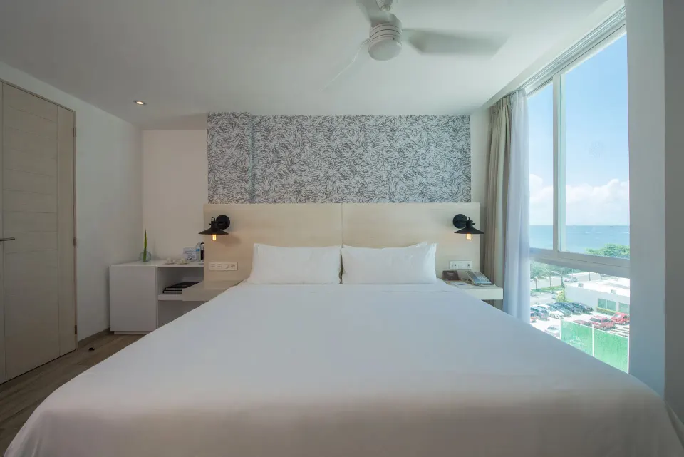 Standard Room king bed beside a large ocean-view window at Oleo Cancun Playa Resort.