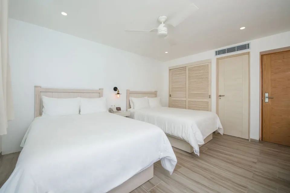 Standard Room with two white beds and closet doors at Oleo Cancun Playa Resort.