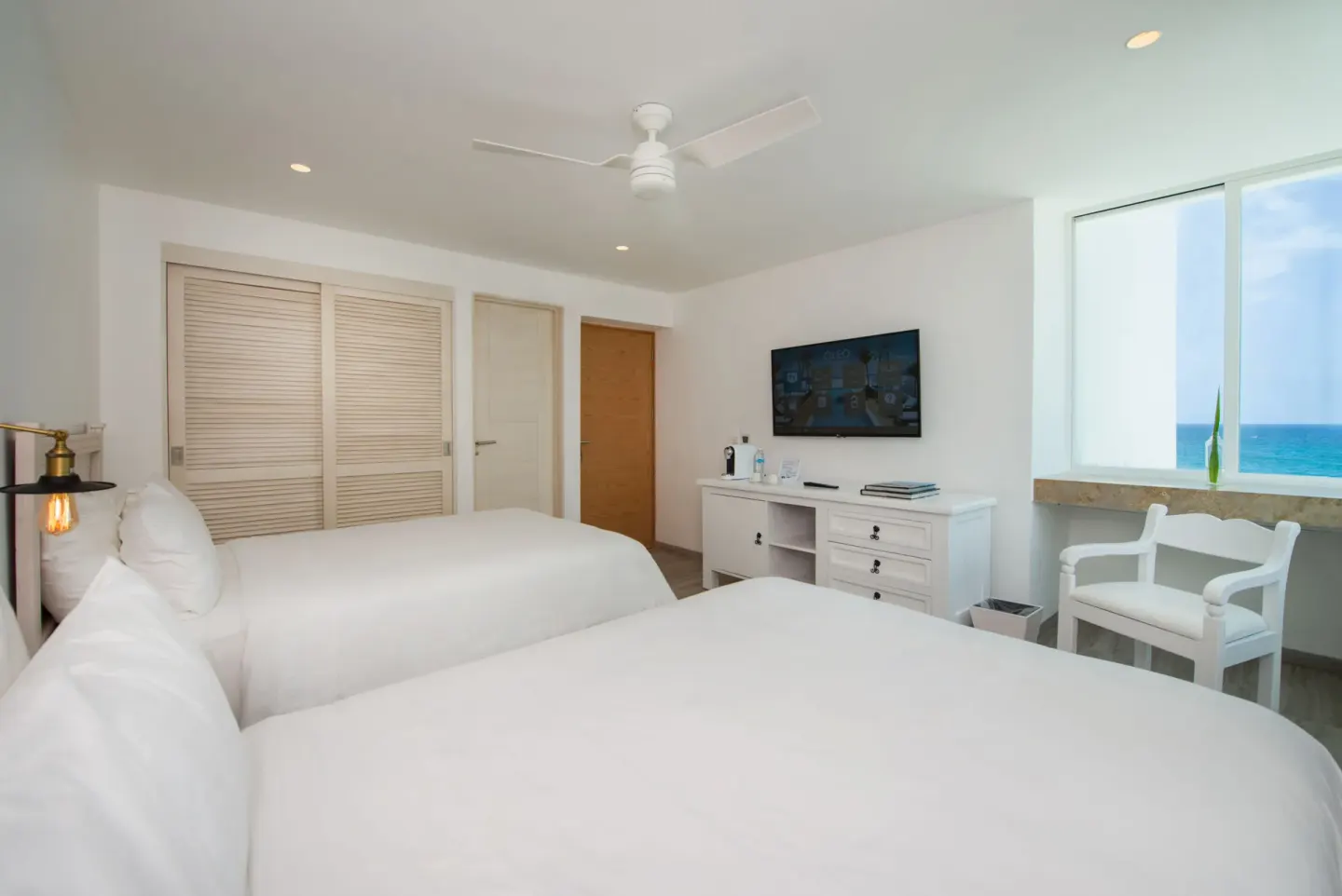 Standard Room with two beds, TV, and ocean-facing window at Oleo Cancun Playa Resort.