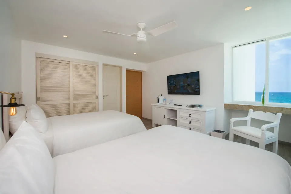 Standard Room with two beds, TV, and ocean-facing window at Oleo Cancun Playa Resort.