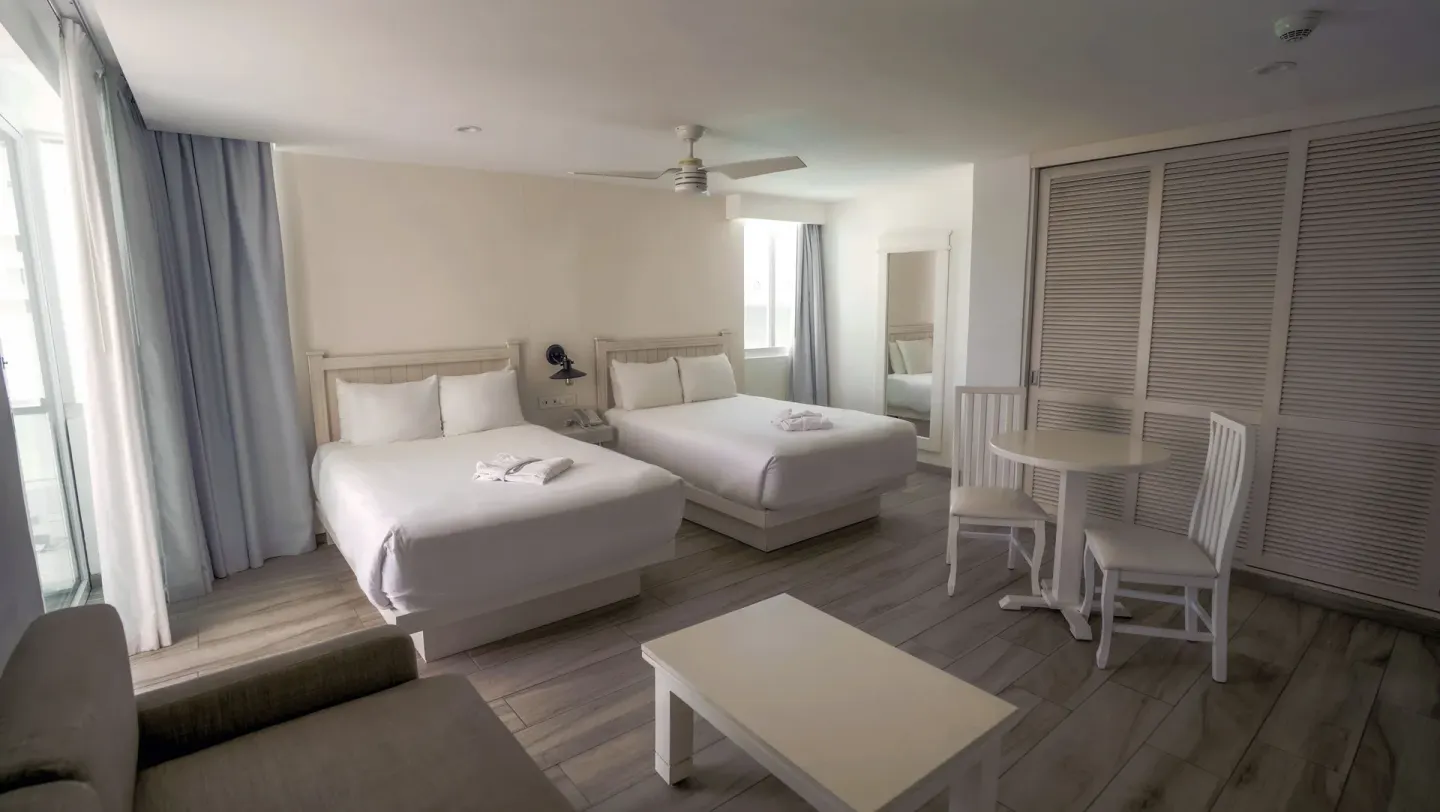 Superior Sunset room with two double beds, table, and closet doors at Oleo Cancun Playa Resort.
