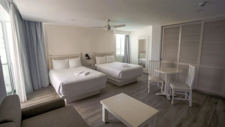Superior Sunset room with two double beds, table, and closet doors at Oleo Cancun Playa Resort.