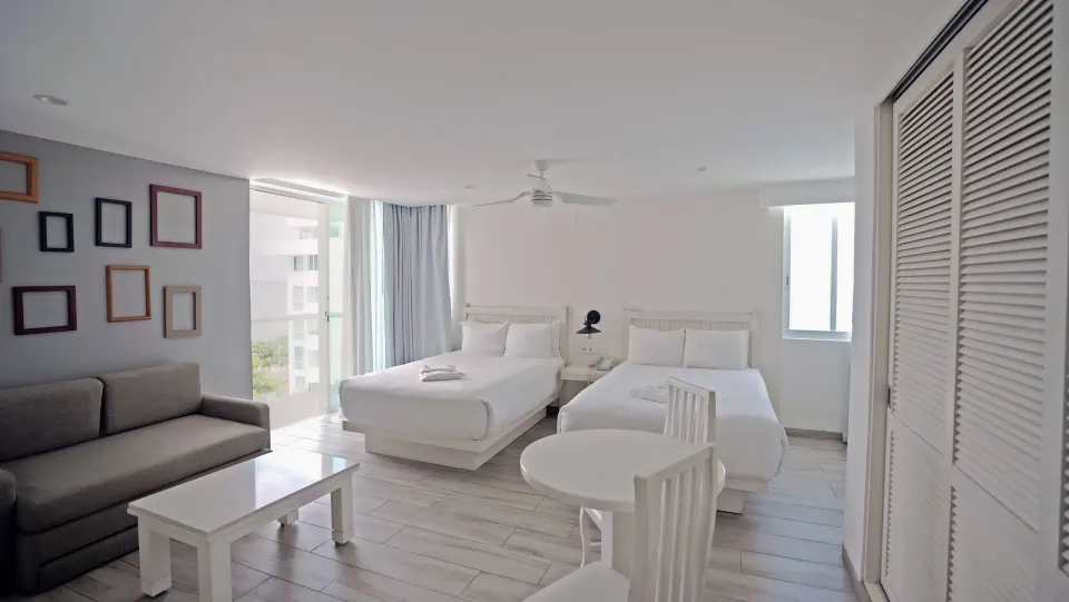 Superior Sunset room with two double beds, sofa, and dining table at Oleo Cancun Playa Resort.