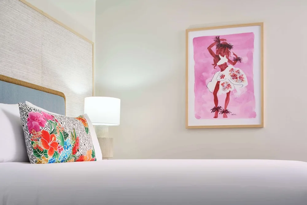 Guest room bed with floral pillow and pink wall art at Outrigger Kaanapali Beach Resort.