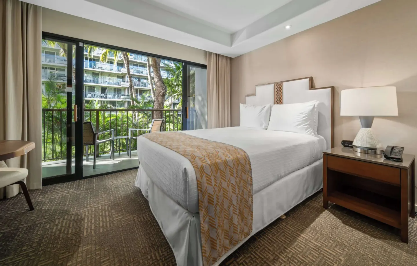 King bed guest room with balcony and tropical greenery at Outrigger Kaanapali Beach Resort.