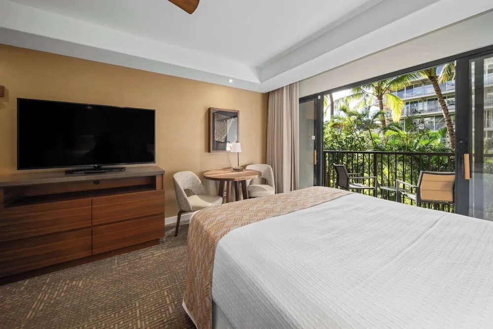 Guest room with king bed, TV, table, and balcony at Outrigger Kaanapali Beach Resort.