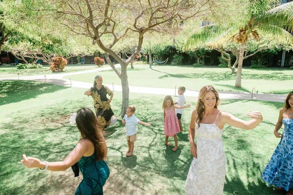 Guests dance on a sunny lawn among trees at Outrigger Kaanapali Beach Resort.