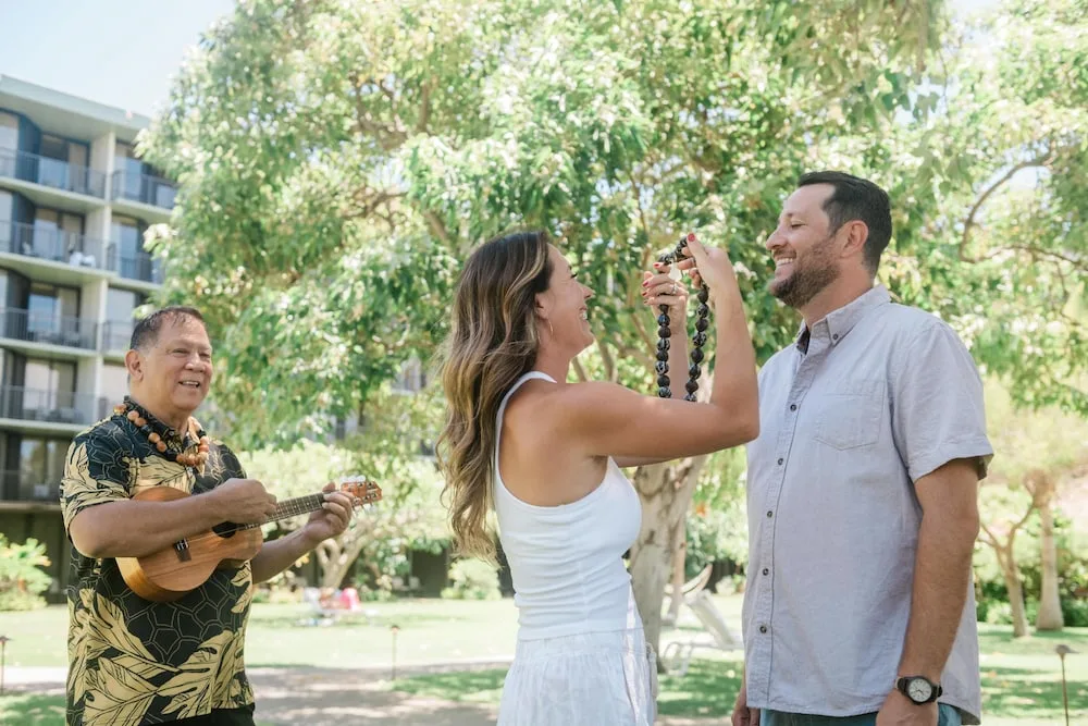 A guest receives a lei as a musician plays ukulele at Outrigger Kaanapali Beach Resort.