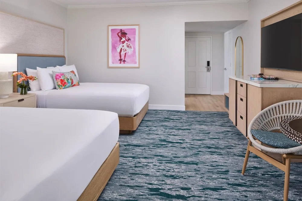 Two-queen guest room with TV, dresser and woven chair at Outrigger Kaanapali Beach Resort.