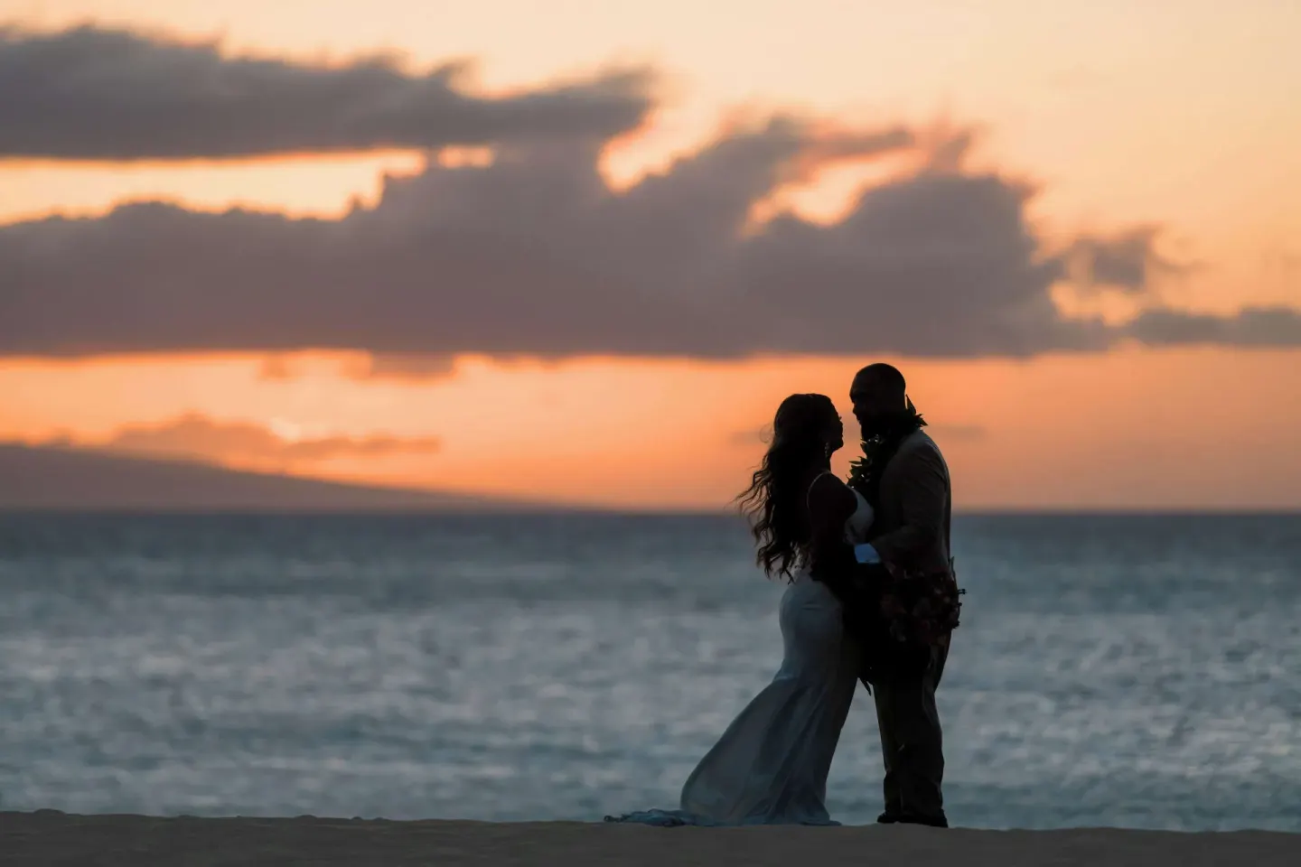 A wedding couple silhouetted by the ocean at sunset at Outrigger Kaanapali Beach Resort.