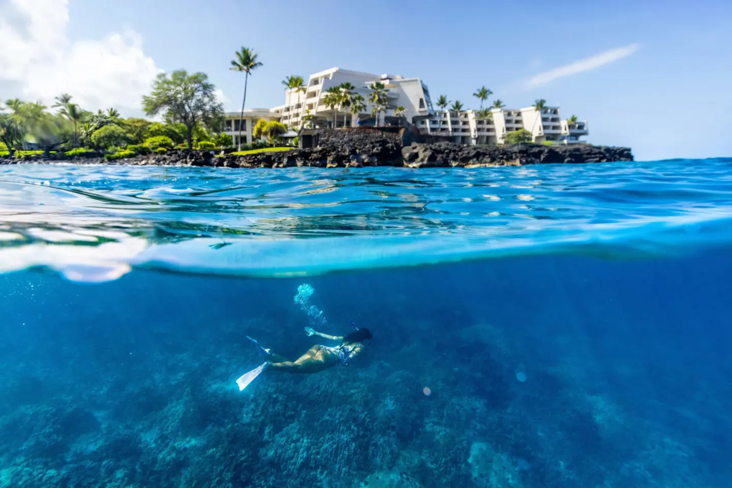 Snorkeler in clear ocean water below Outrigger Kona Resort and Spa.
