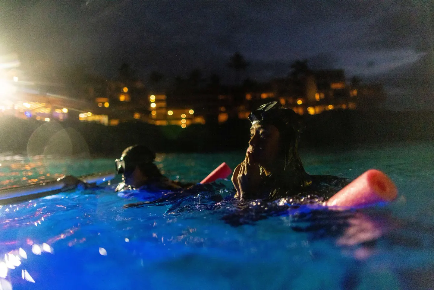 Night snorkelers floating in illuminated ocean water at Outrigger Kona Resort and Spa.