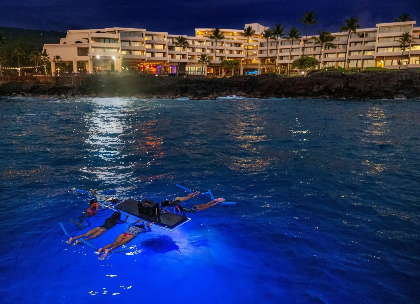 Night snorkelers in blue-lit water offshore from Outrigger Kona Resort and Spa.