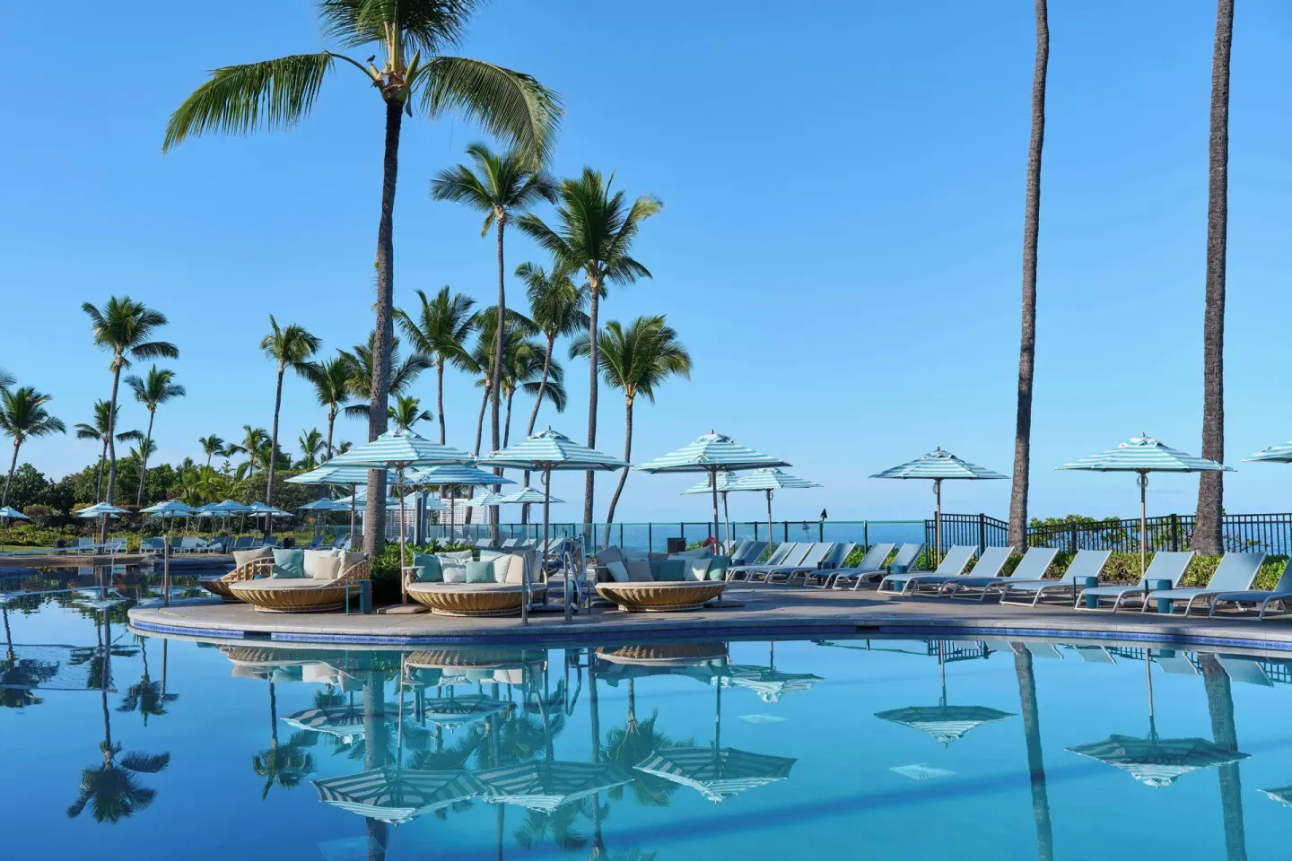 Pool loungers, umbrellas, and palm trees by the ocean at Outrigger Kona Resort and Spa.