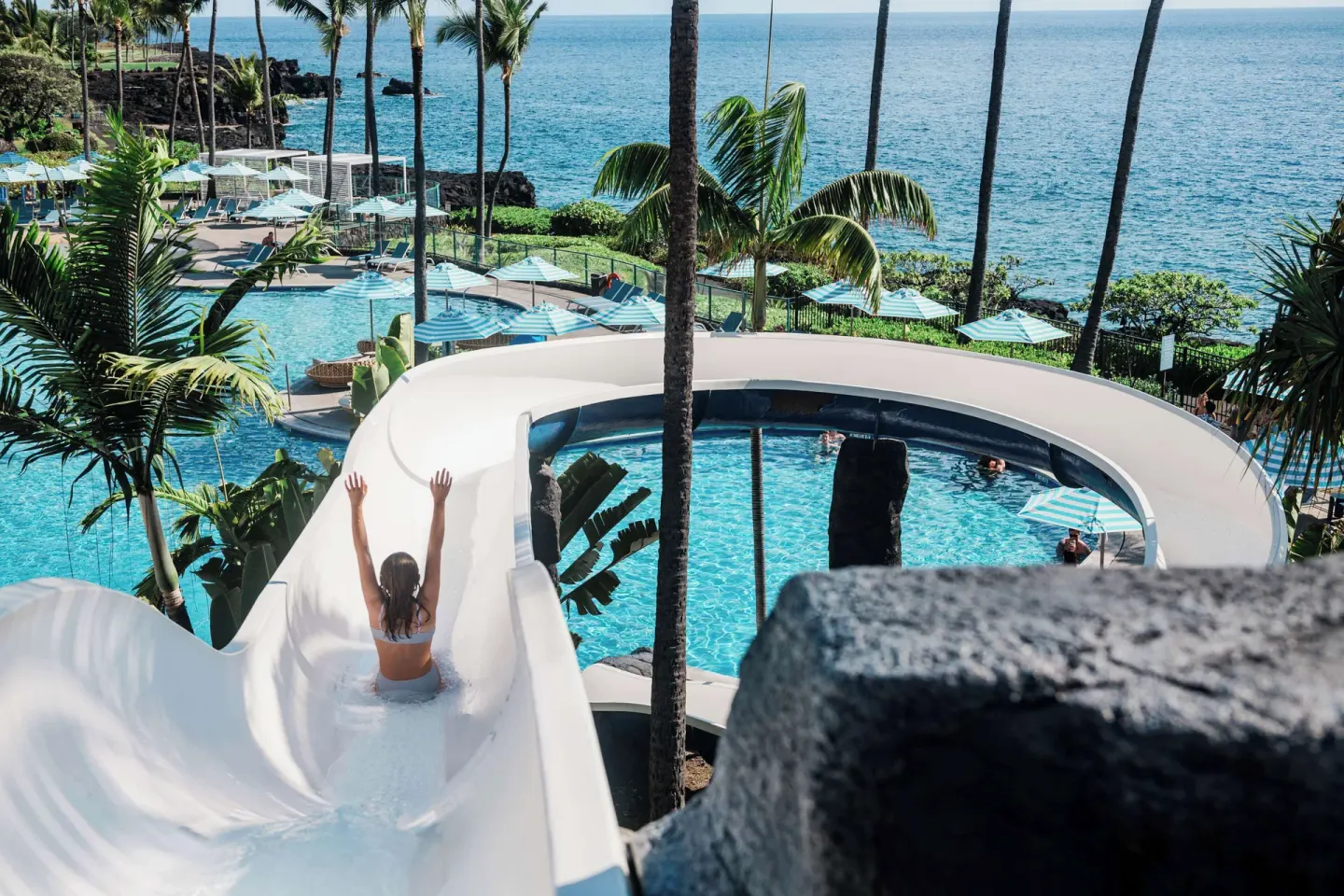 Guest rides a white waterslide above the oceanfront pool at Outrigger Kona Resort and Spa.
