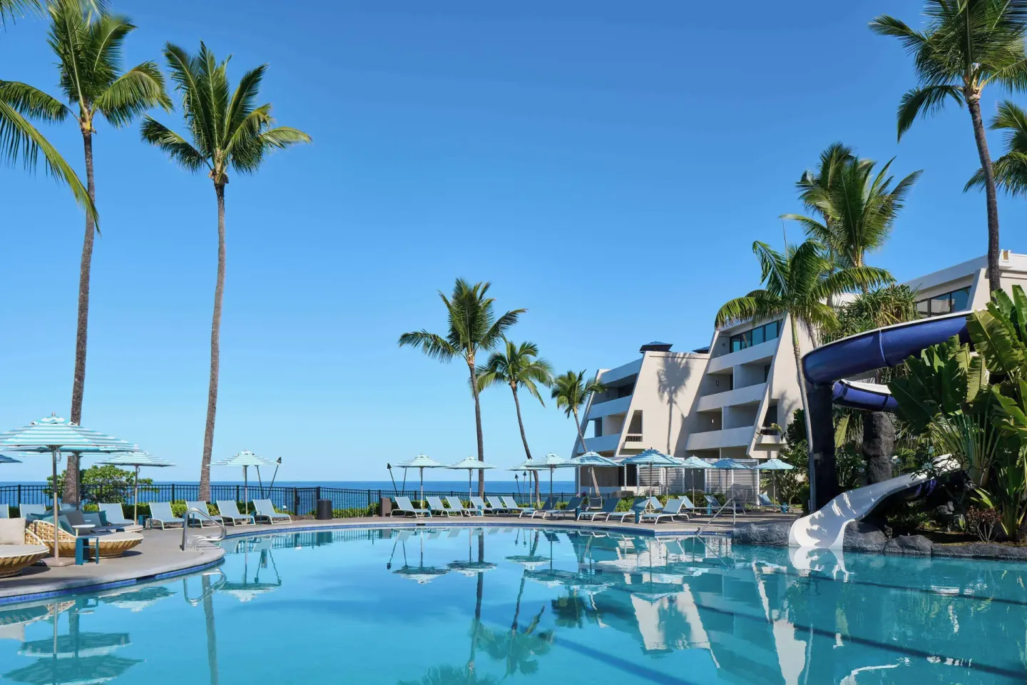 A resort pool with a waterslide, palms, and ocean views at Outrigger Kona Resort and Spa.