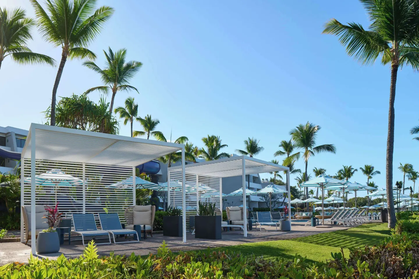 Poolside cabanas and lounge chairs among palms at Outrigger Kona Resort and Spa.
