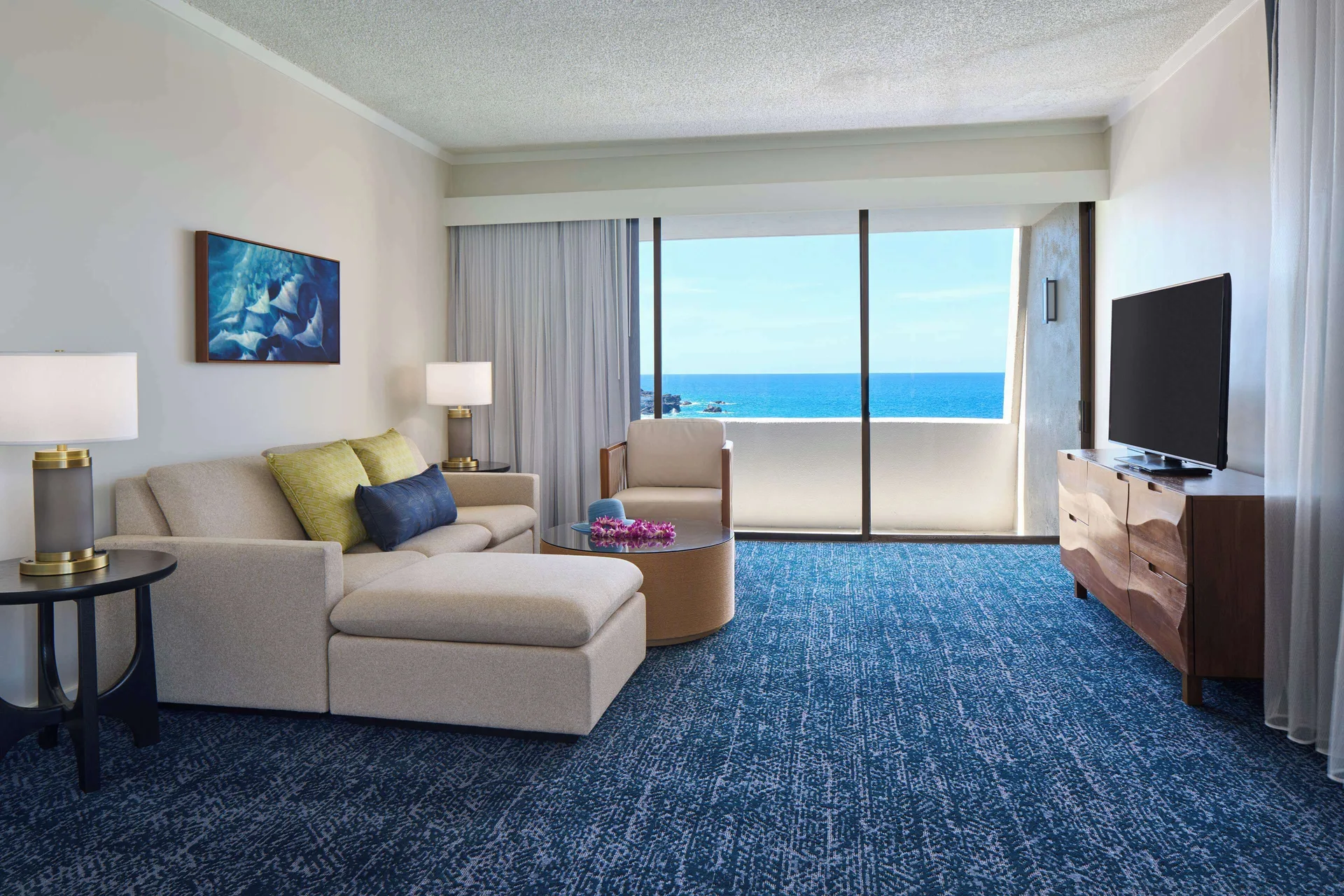 Deluxe Ocean Front Suite living room with sofa, TV and balcony view at Outrigger Kona Resort and Spa.