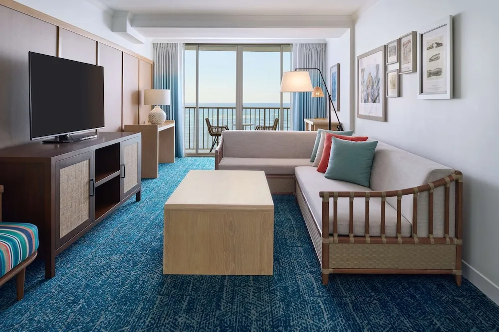 Suite living room with sofa, TV, and ocean balcony at OUTRIGGER Reef Waikiki Beach Resort.