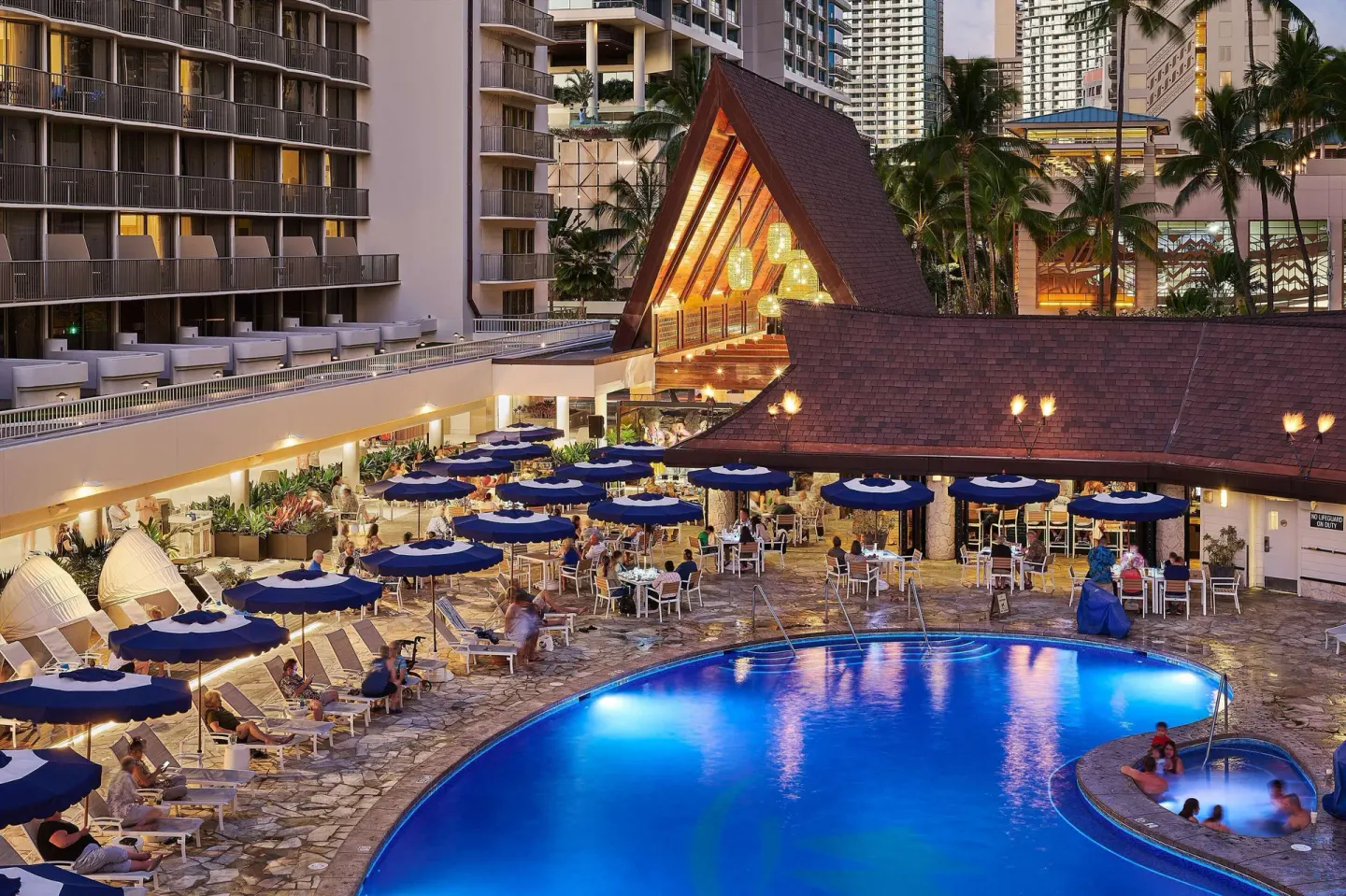 Pool courtyard and dining tables at dusk at OUTRIGGER Reef Waikiki Beach Resort.