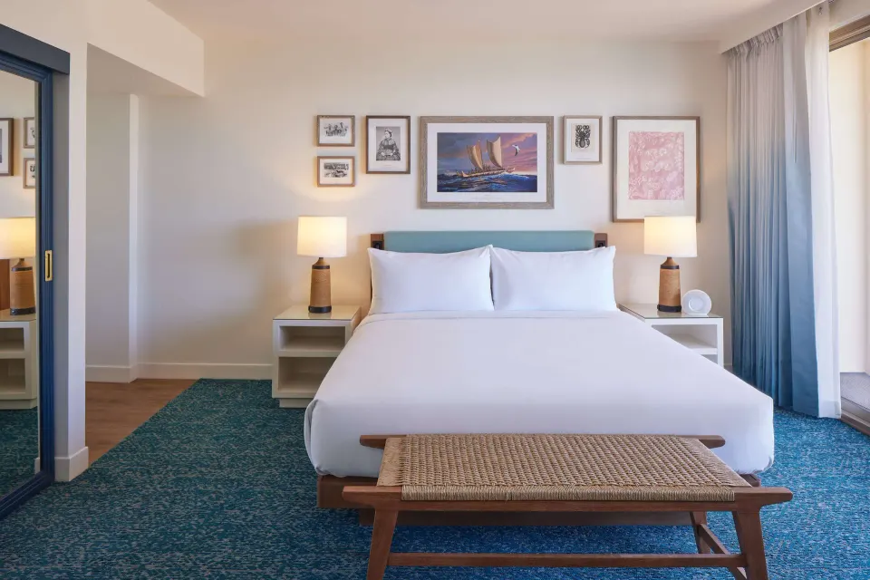 Grand Navigator Suite king bed with lamps and wall art at OUTRIGGER Reef Waikiki Beach Resort.