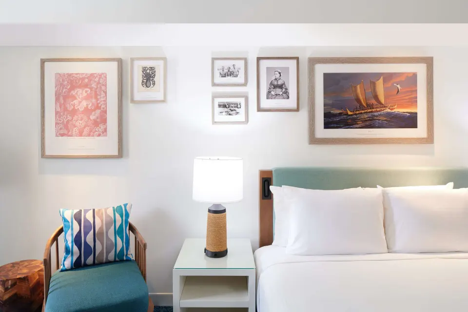 Standard Room bed and chair beneath framed artwork at OUTRIGGER Reef Waikiki Beach Resort.
