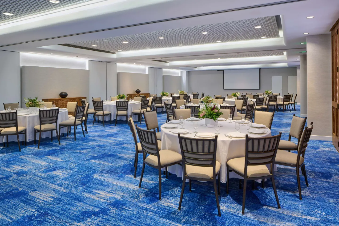Event room with banquet tables and a projection screen at OUTRIGGER Reef Waikiki Beach Resort.